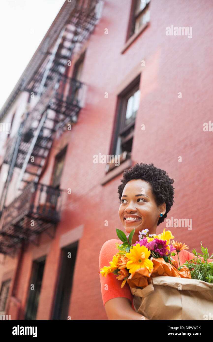 Woman carrying bag of flowers on city street Stock Photo