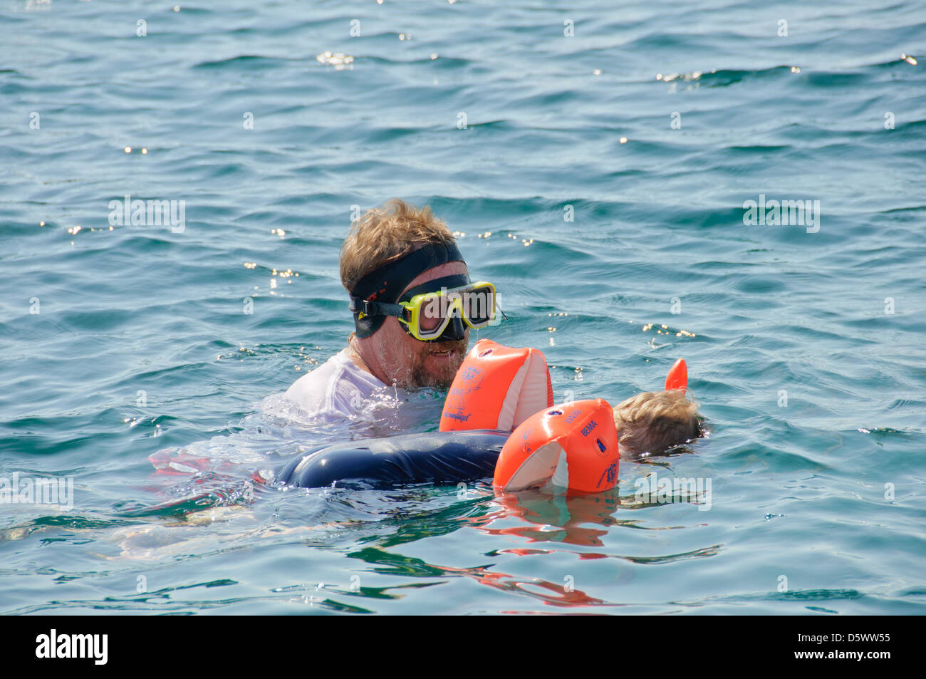 Little Caucasian blond boy swims with his father in the ocean wearing