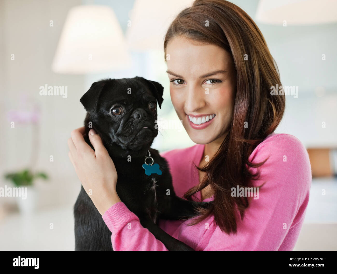 Smiling woman holding dog indoors Stock Photo