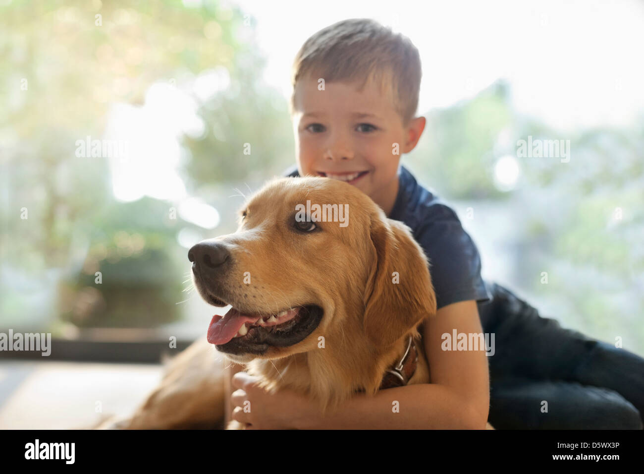 Smiling boy hugging dog indoors Stock Photo