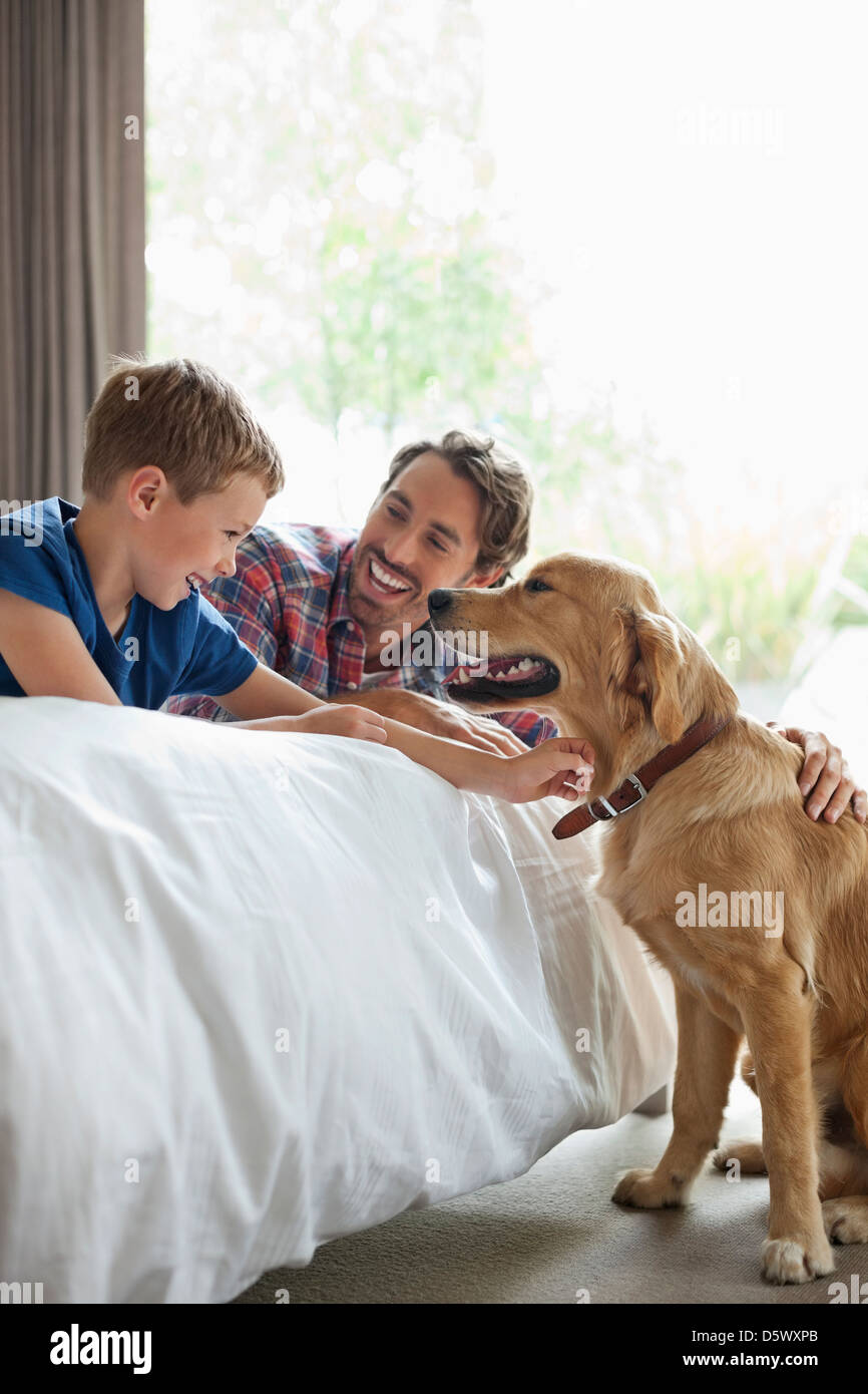 Father and son petting dog in bedroom Stock Photo