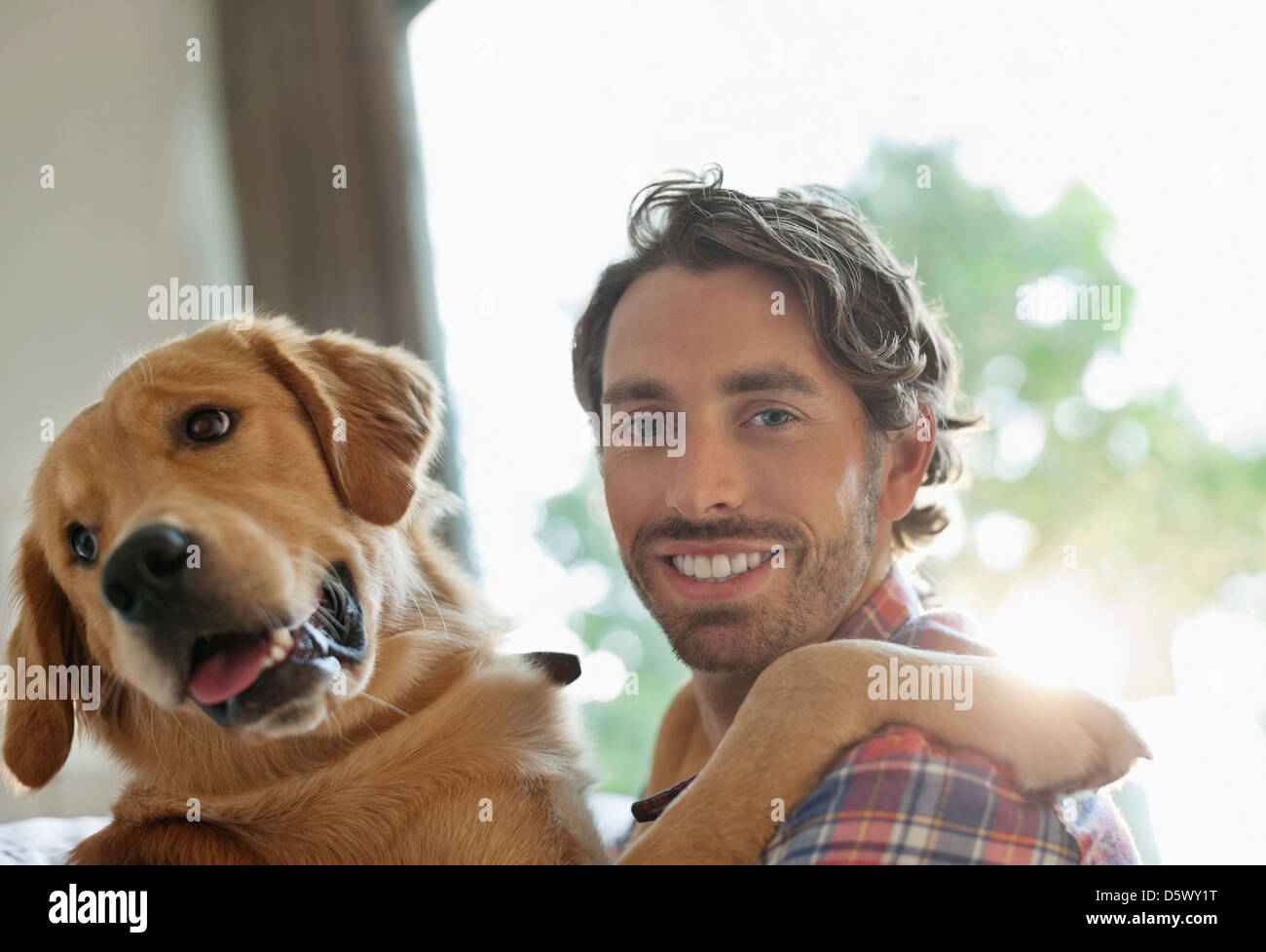 Smiling man petting dog indoors Stock Photo