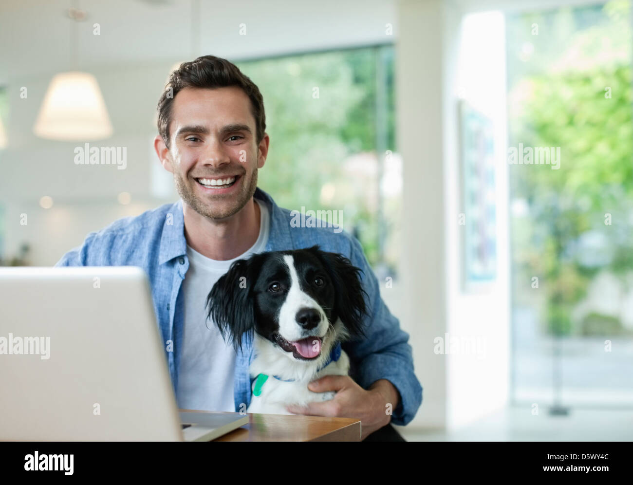 Man with dog using laptop in kitchen Stock Photo