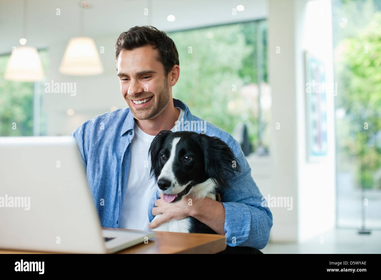 Man with dog on lap using laptop Stock Photo