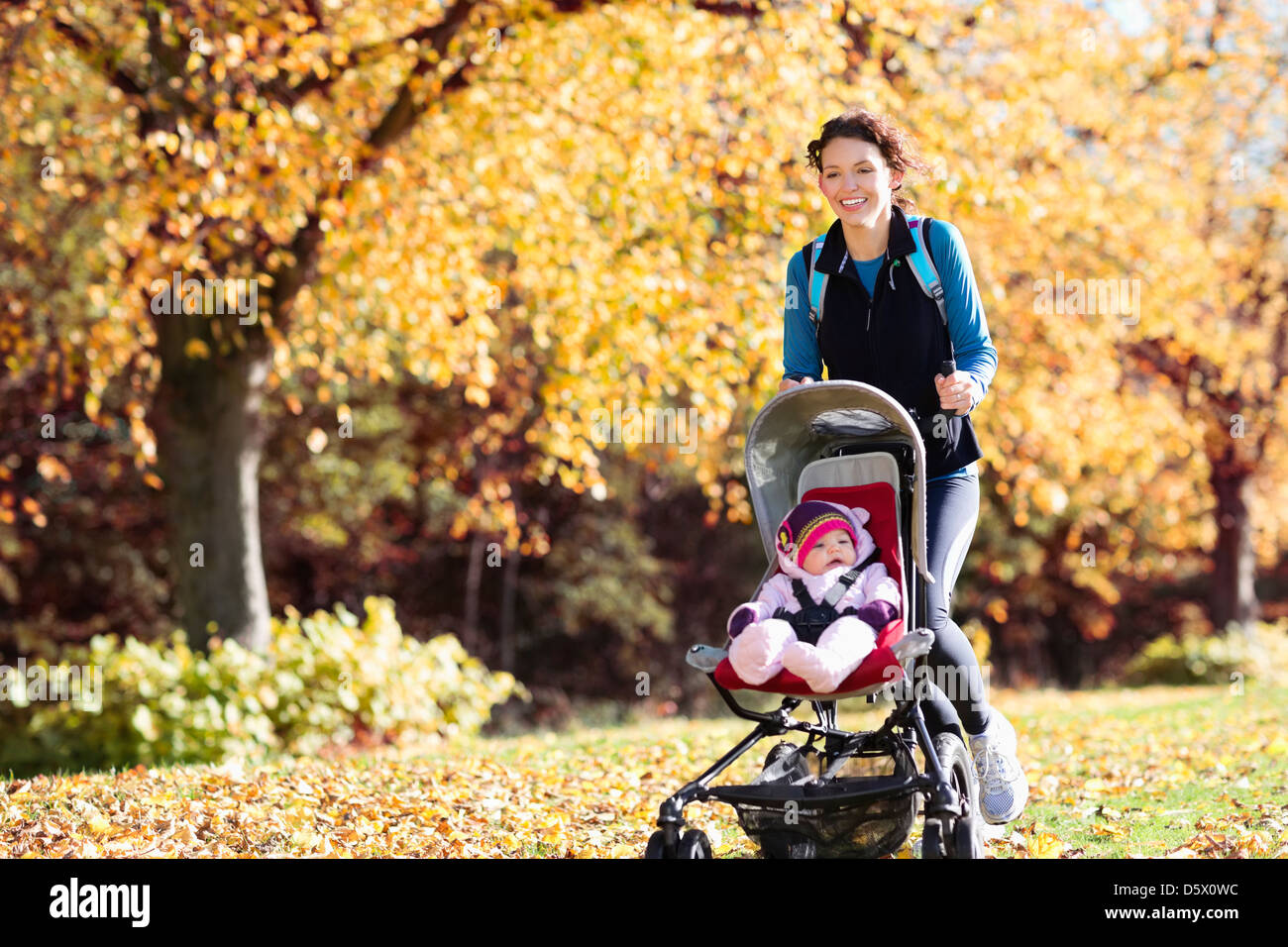 Woman running with baby stroller in park Stock Photo