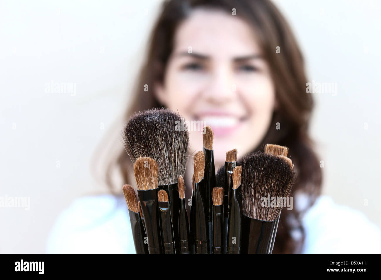Happy young Woman showing a variety of makeup brushes Stock Photo