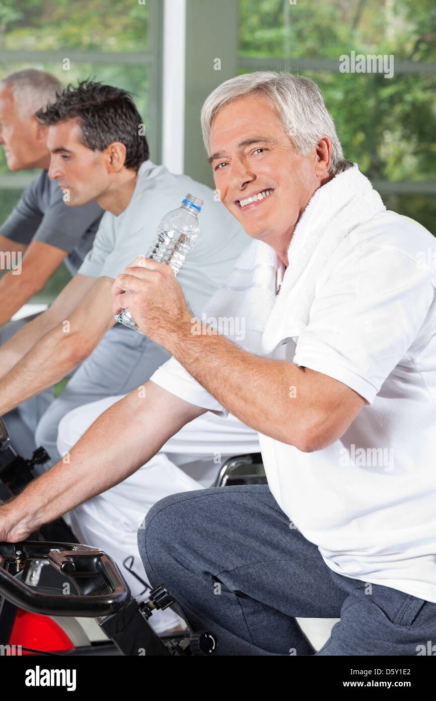 Smiling senior with water bottle in gym on bike Stock Photo - Alamy