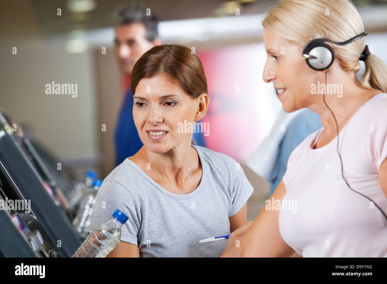 Fitness trainer talking to senior woman on treadmill in gym Stock Photo