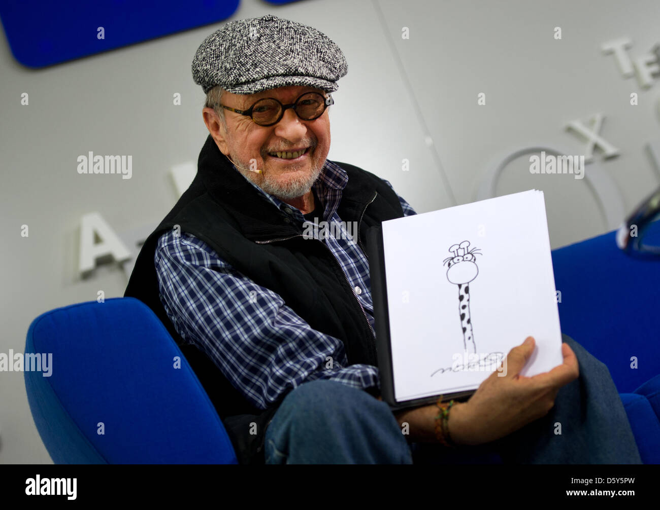 Argentinian artist Guillermo Mordillo sits on the book fair's 'blue sofa' holding the drawing of a giraffe at the Book Fair in Frankfurt am Main, Germany, 13 October 2012. Mordillo presents his book '4 x 20 Jahre jung' (lit. '4 times 20 years old'). Photo: Arno Burgi Stock Photo