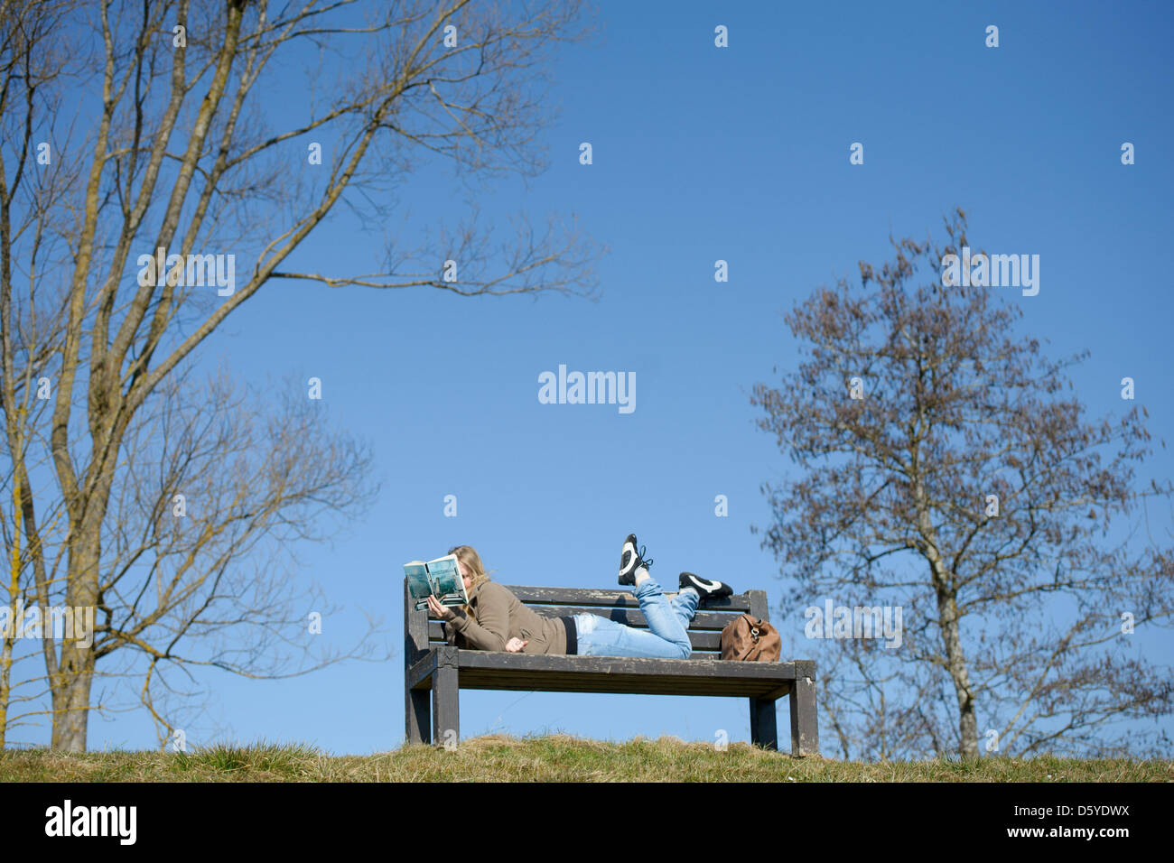A young woman lies on a bench and reads a book in Pfullendorf, Germany, 16 March 2012. Photo: Tobias Kleinschmidt Stock Photo