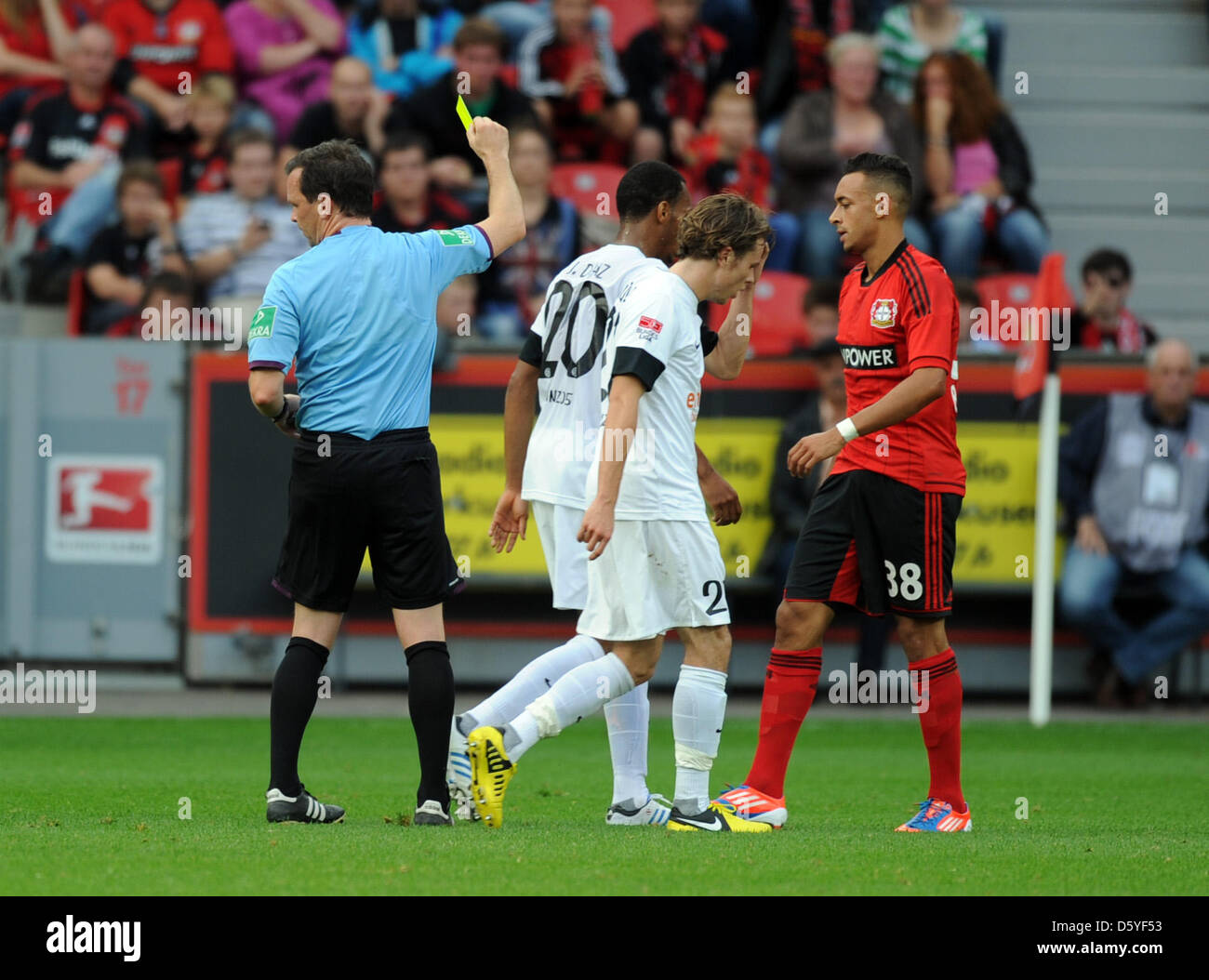 Referee Peter Sippel (L) shows the yellow card to Leverkusen's Karim