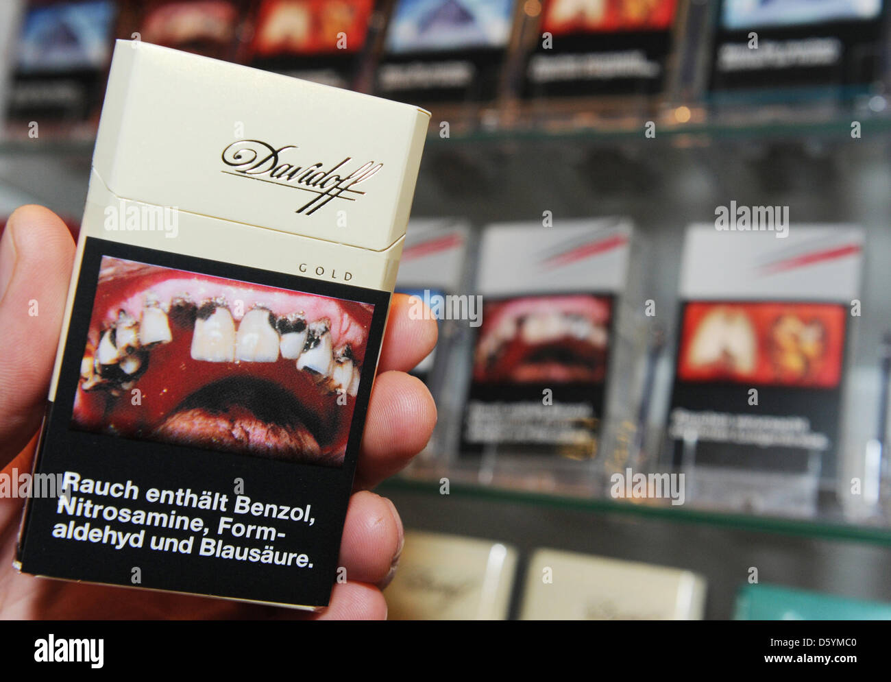 A hand holds a packet of cigarettes in front of Products of the tobacco and cigarette company Reemtsma which are illustrated with repulsive photos pictured during the company's financial statements press conference in Hamburg, Germany, 30 October 2012. Reemtsma wishes to call attention to the European Union directives which could lead to the expropriation of their brands and compan Stock Photo