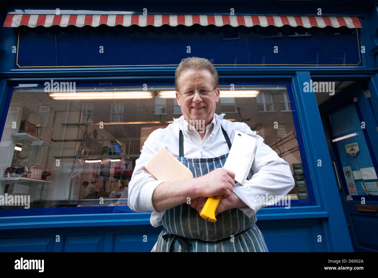 Portrait of happy senior butcher standing with crossed cleavers in
