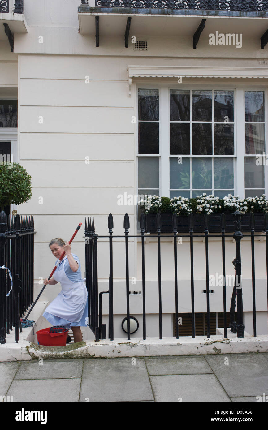 A maid uses a mop and bucket to wash down paintwork and railings at an