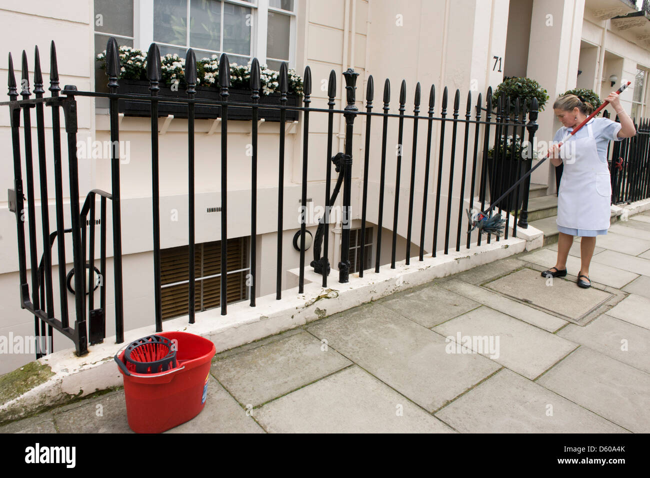 A maid uses a mop and bucket to wash down paintwork and railings at an