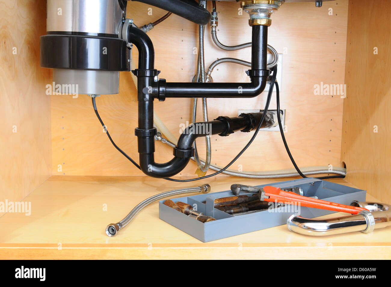Detail of the plumbing system under a modern kitchen sink, with a plumbers tool tray and equipment. Horizontal format. Stock Photo