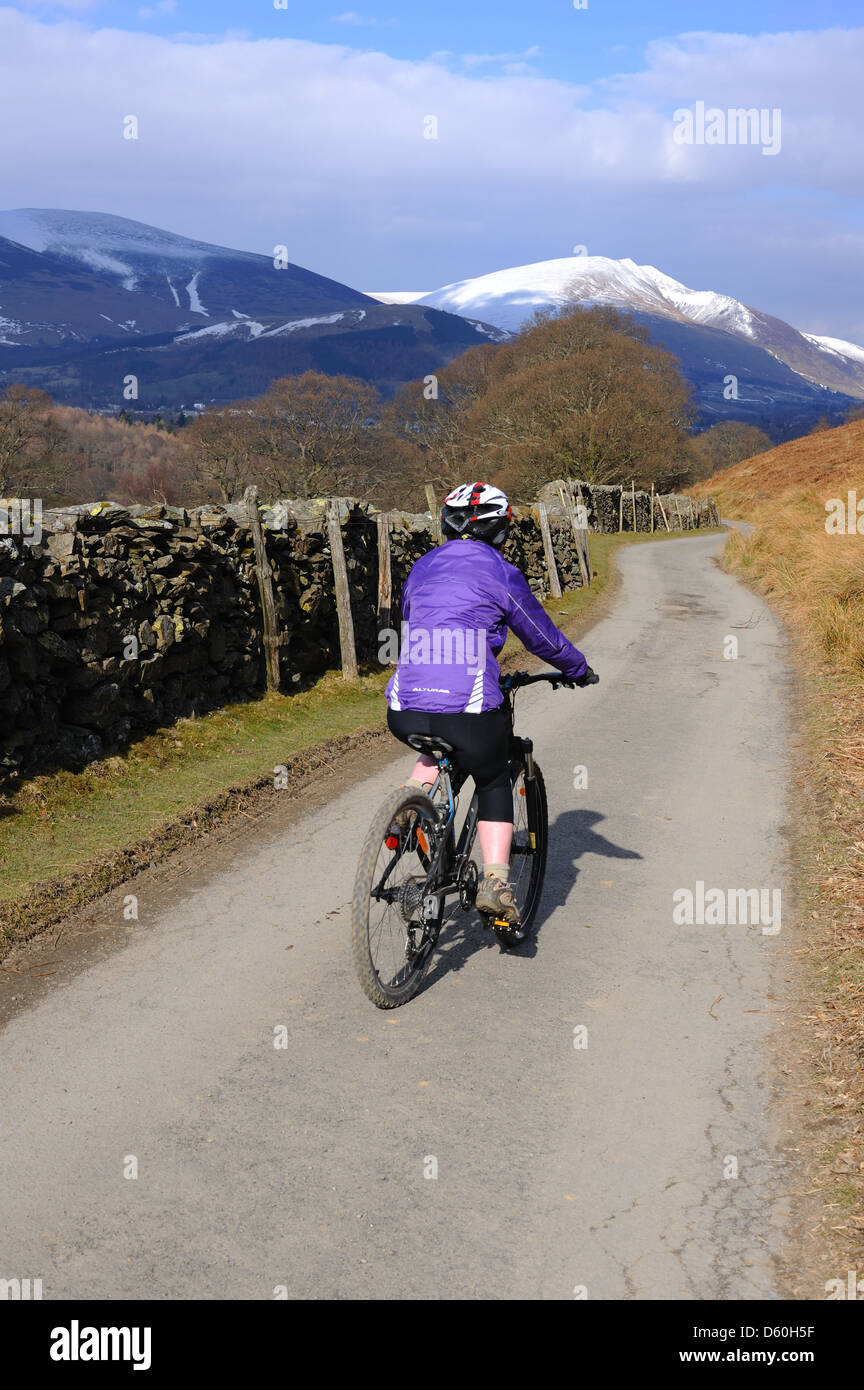 Lady cycling on a Lakeland road with Blencathra in the distance Stock Photo