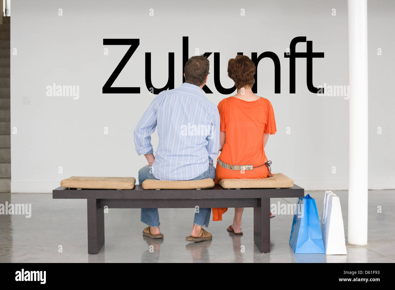 Rear view of couple seated bench reading German text 'Zukunft' (future) wall Stock Photo