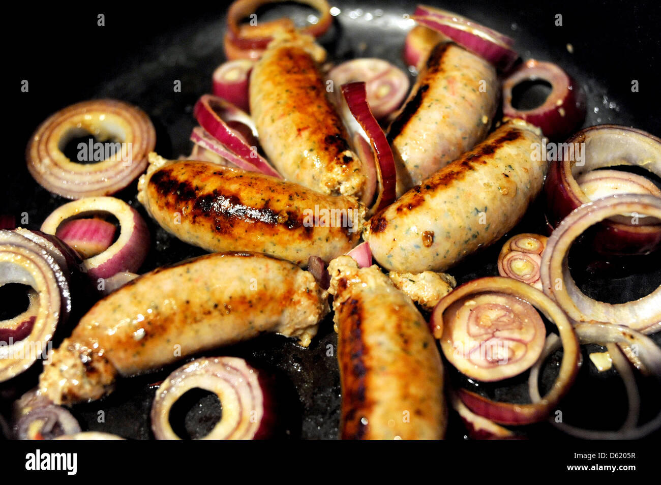 Pork sausages sizzling in a frying pan with red onions as they are