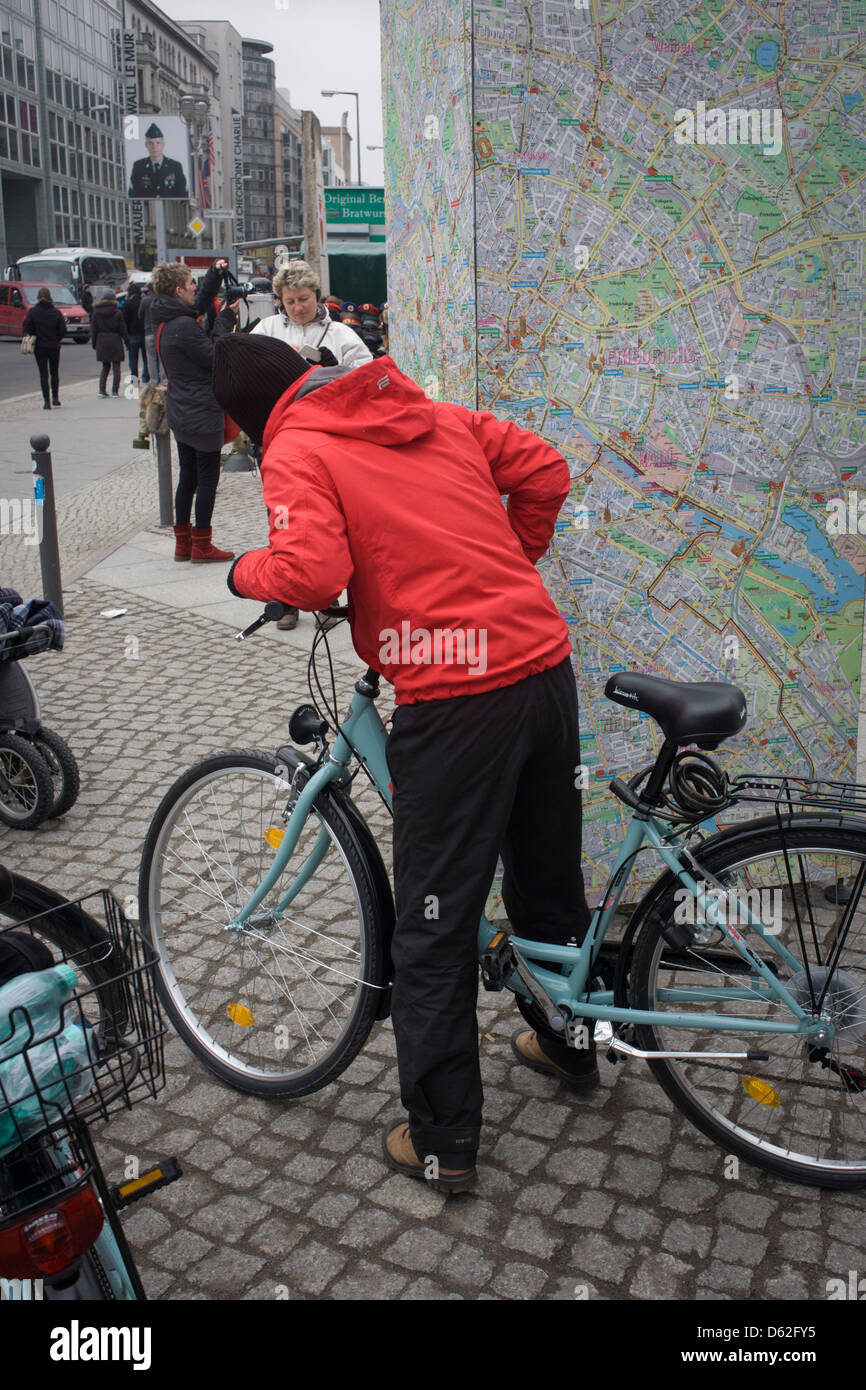A cyclist stops to read a map of Berlin near the former Checkpoint Charlie, the former border between Communist East and West Berlin during the Cold War. Many cycling rental companies operate in the city where pavements and streets include cycle lanes. Stock Photo