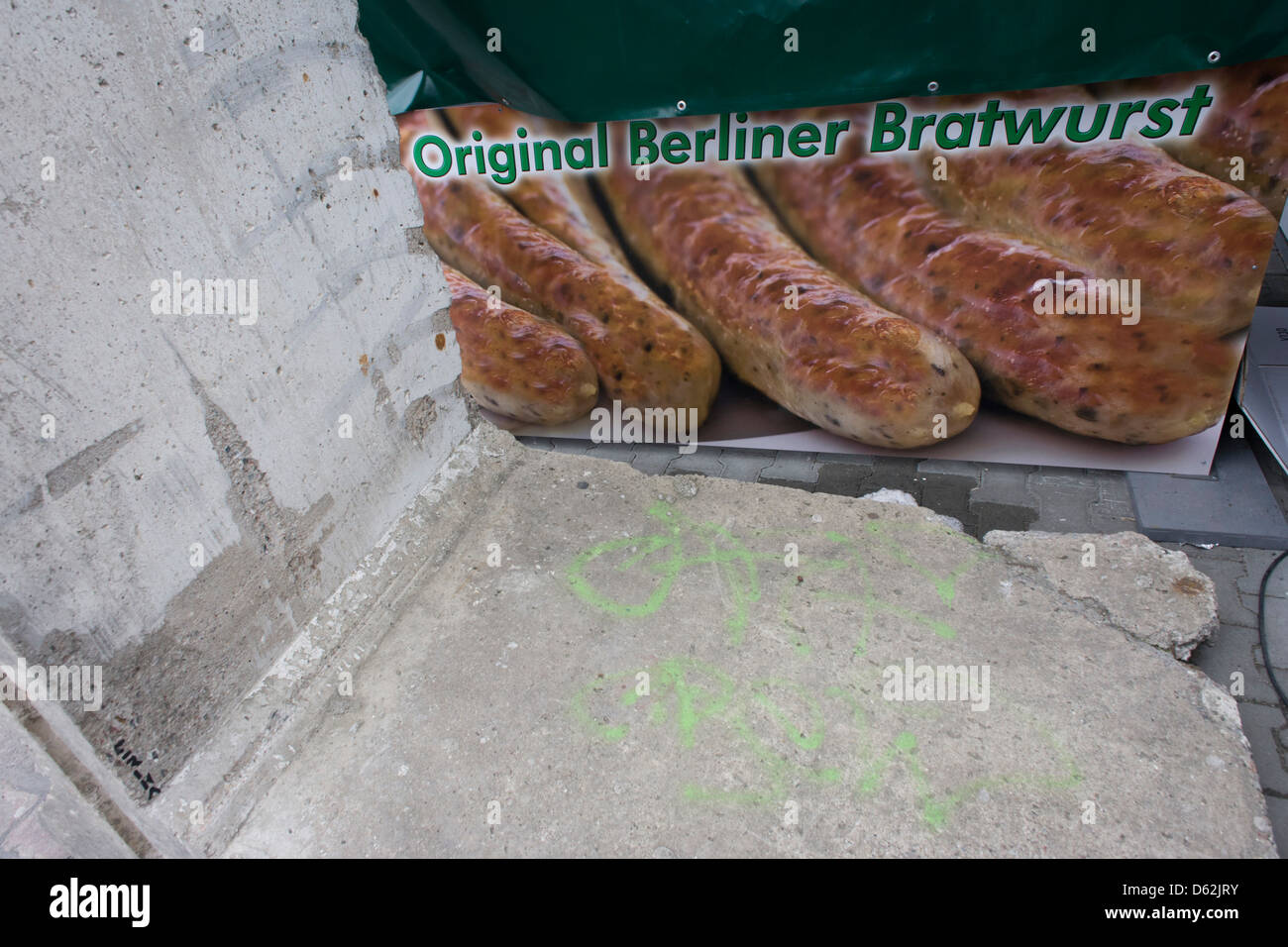 A poster for original Berliner Bratwurst sausage next to a section of the Berlin wall near the former Checkpoint Charlie, the former border between Communist East and West Berlin during the Cold War. The Berlin Wall was a barrier constructed by the German Democratic Republic (GDR, East Germany) starting on 13 August 1961, that completely cut off (by land) West Berlin from surrounding East Germany and from East Berlin.  .. (More in Description). Stock Photo