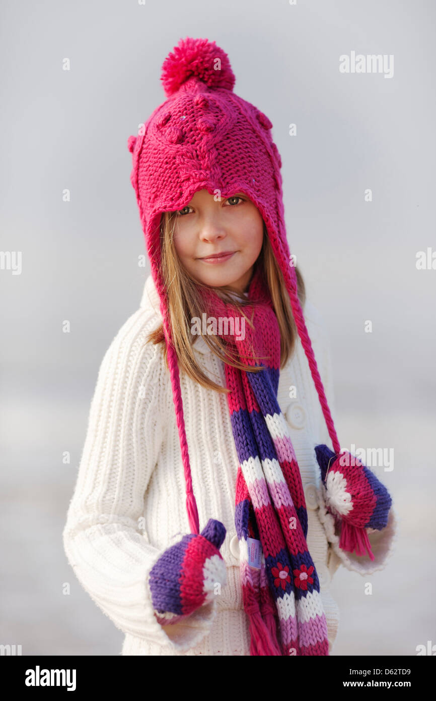 Portrait of a cute young girl in pink hat and Winter clothing on beach ...