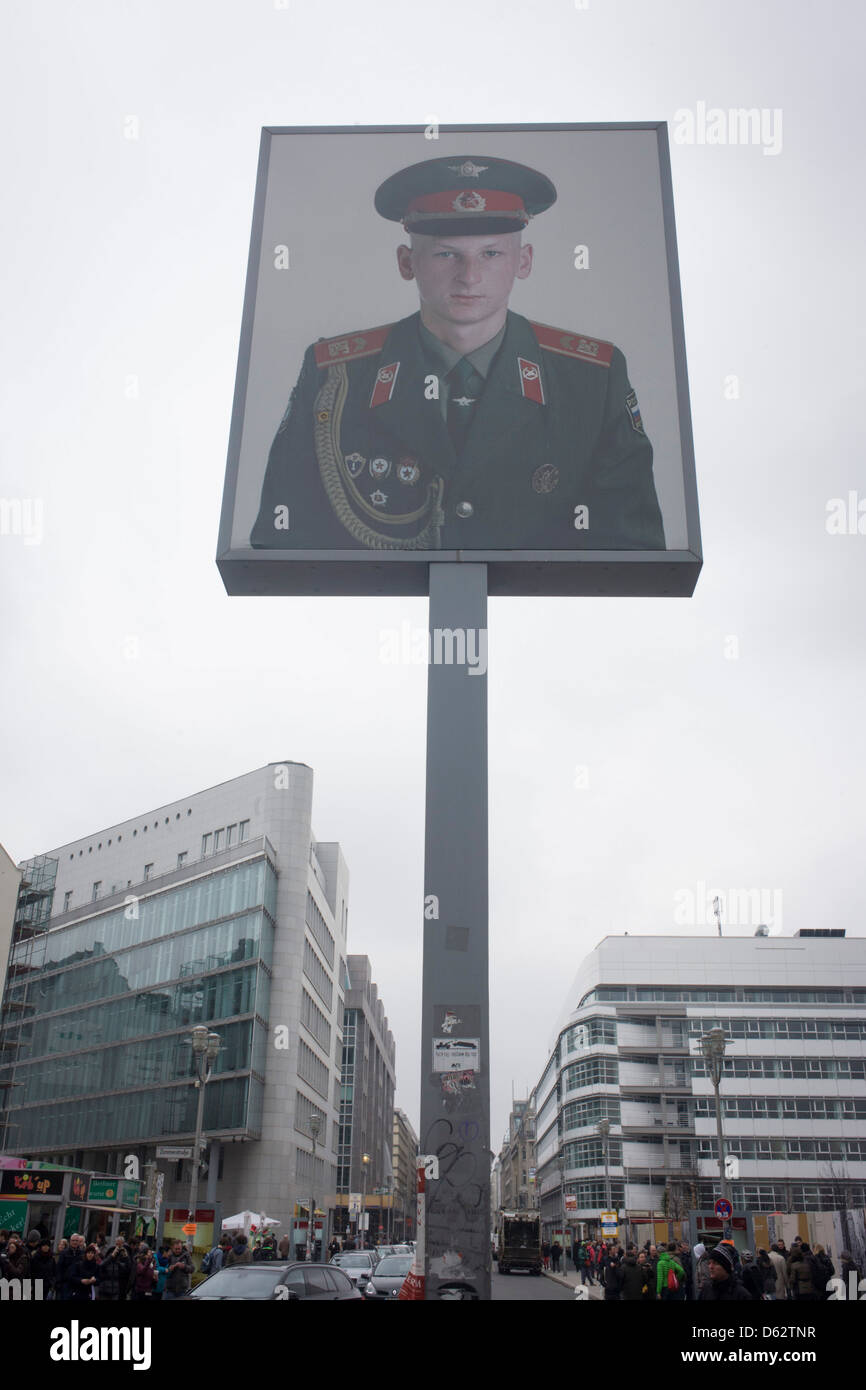 The portrait of a Soviet soldier sits high above modern Friedrishstrasse in modern Berlin at the location of the former Checkpoint Charlie, the former border between Communist East and West Berlin during the Cold War. The Berlin Wall was a barrier constructed by the German Democratic Republic (GDR, East Germany) starting on 13 August 1961, that completely cut off (by land) West Berlin from surrounding East Germany and from East Berlin. Stock Photo
