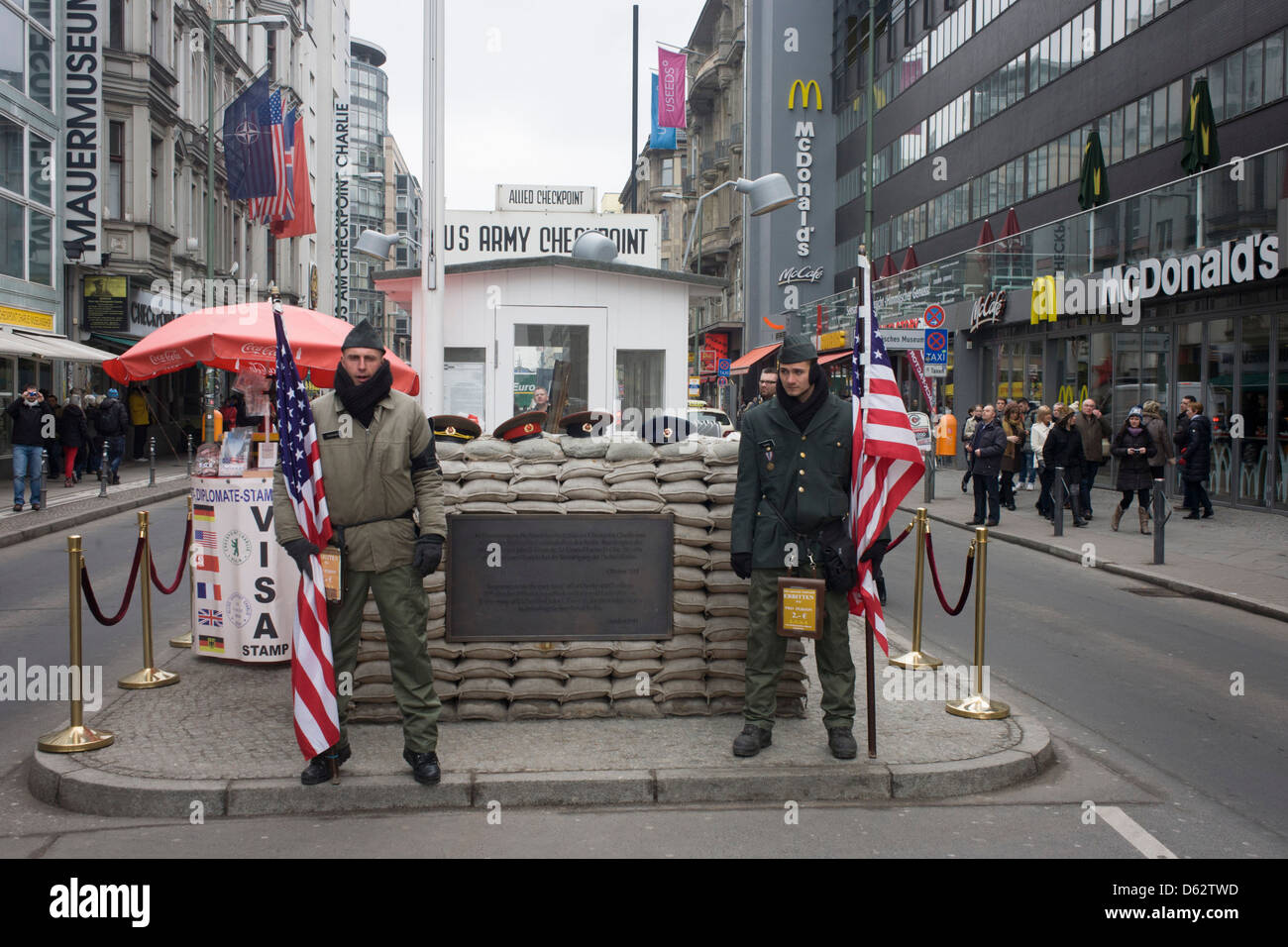 Young men re-enact the former border crossing between Communist East and West Germany during the Cold War at the site of the former Checkpoint Charlie, the border. The Berlin Wall was a barrier constructed by the German Democratic Republic (GDR, East Germany) starting on 13 August 1961, that completely cut off (by land) West Berlin from surrounding East Germany and from East Berlin. (More in Description) .. Stock Photo