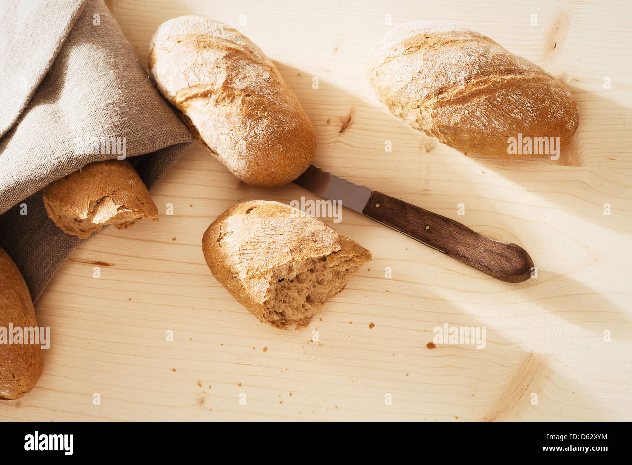 broken rye bun with rye buns and a knife from top on wooden background ...