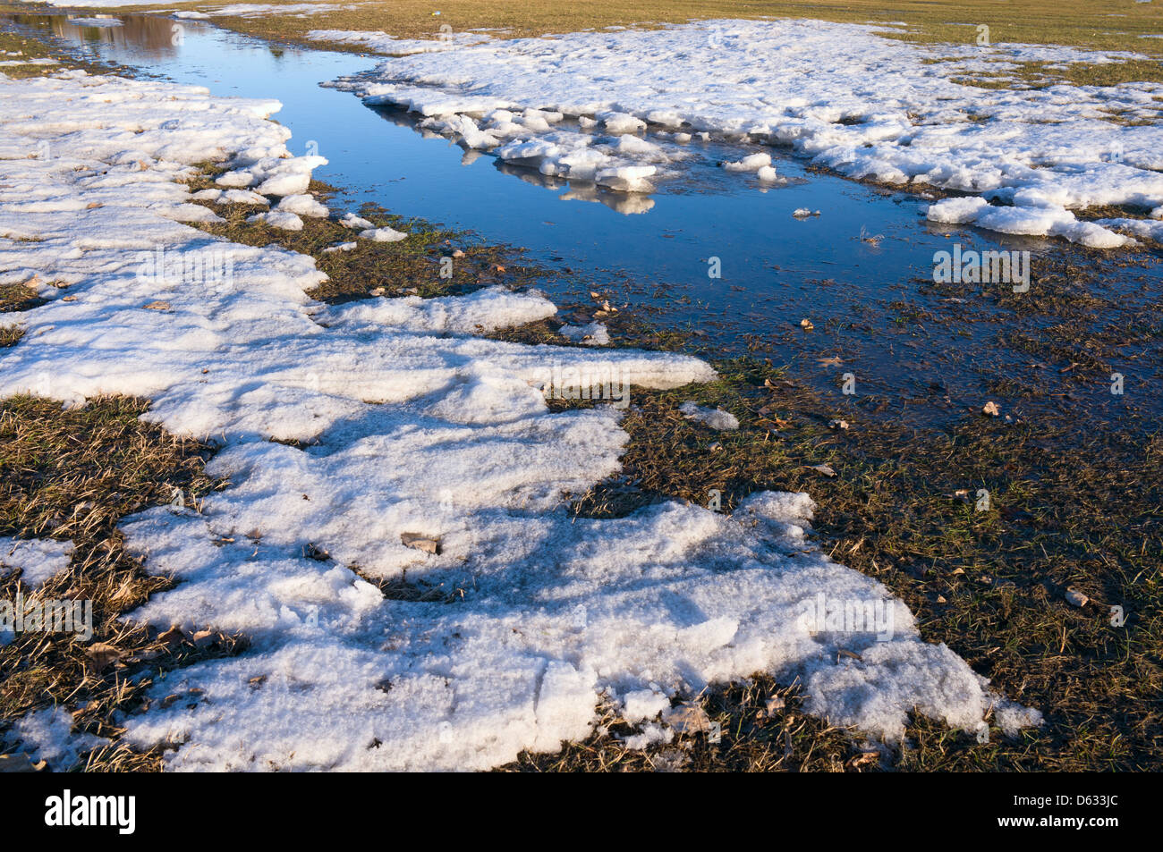 Thawing snow and ice with stream of water reflecting blue sky Stock ...