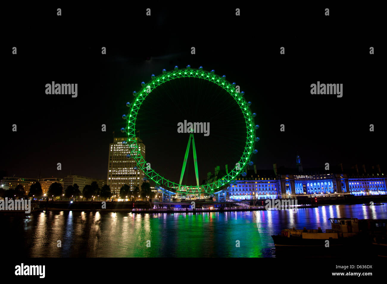 London eye is lit up in green lights, the lights of the Southbank reflect on the river Thames bellow. Stock Photo