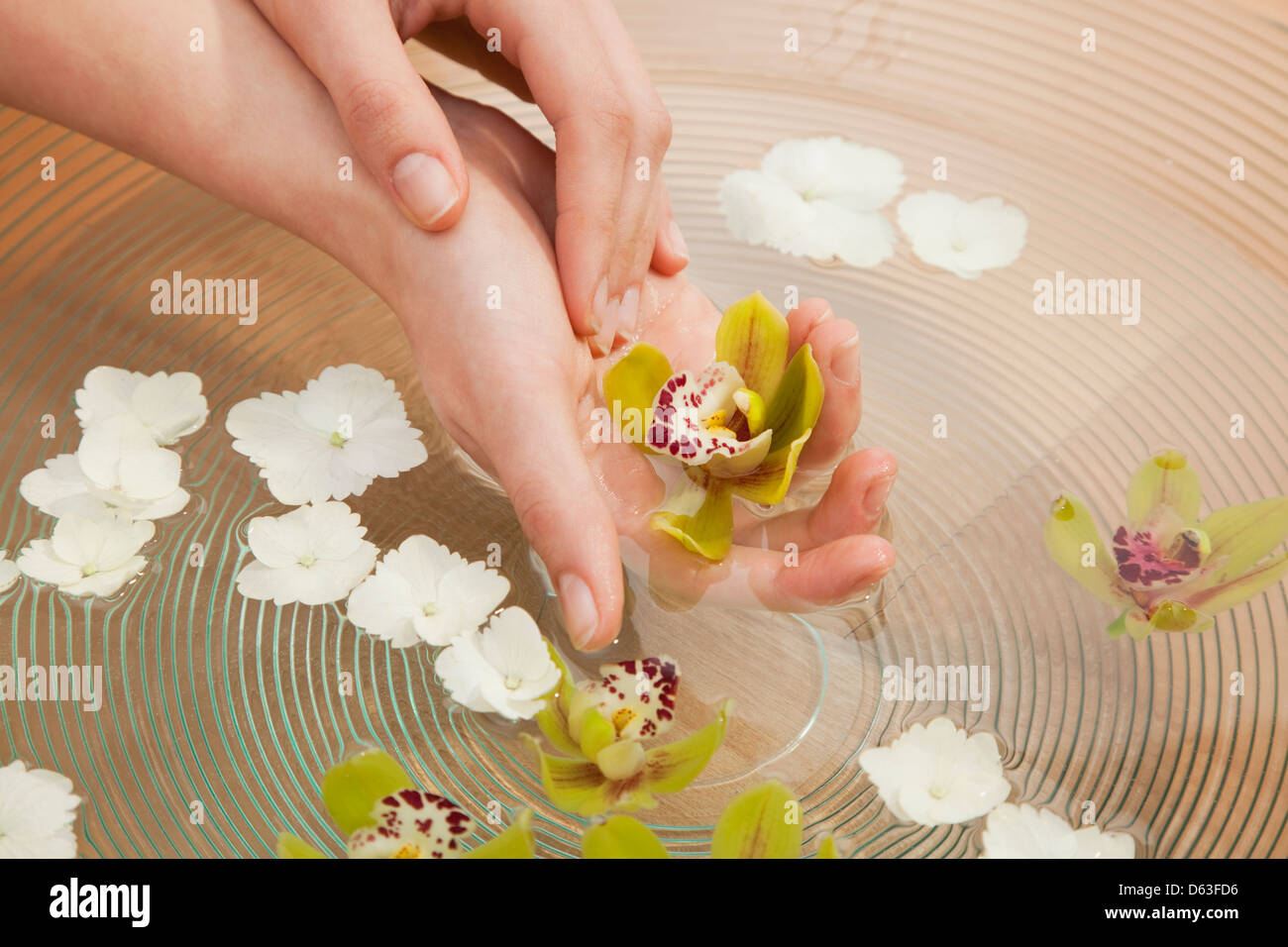 Hands in bowl with clean water and flowers Stock Photo