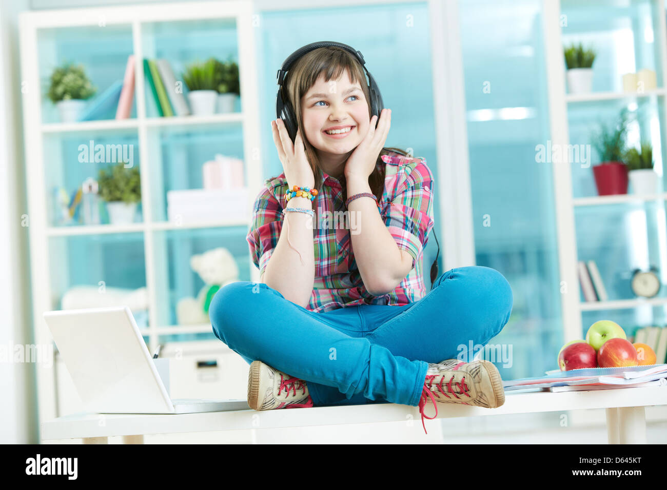 Image of a happy teen girl sitting on the desk and listening to music ...