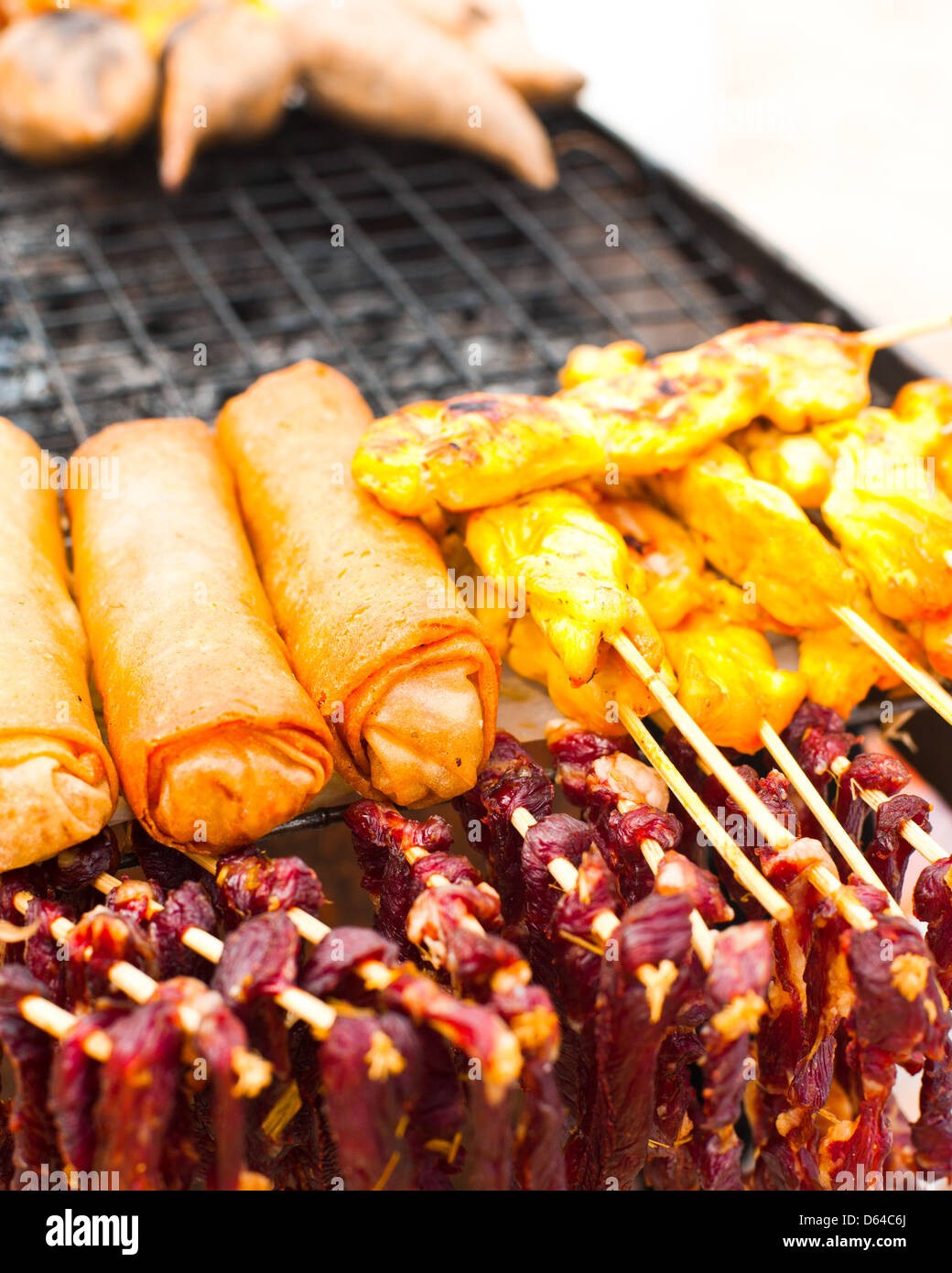 Traditional Thai food at market. Dry beef meat, spring rolls and curry chicken on grill Stock Photo