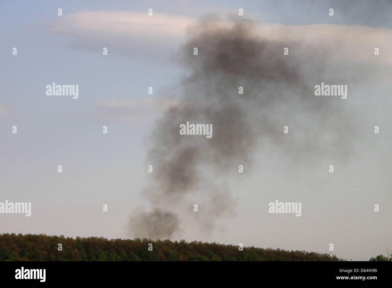 A column of black smoke rising over a dense green forest, indicating a ...