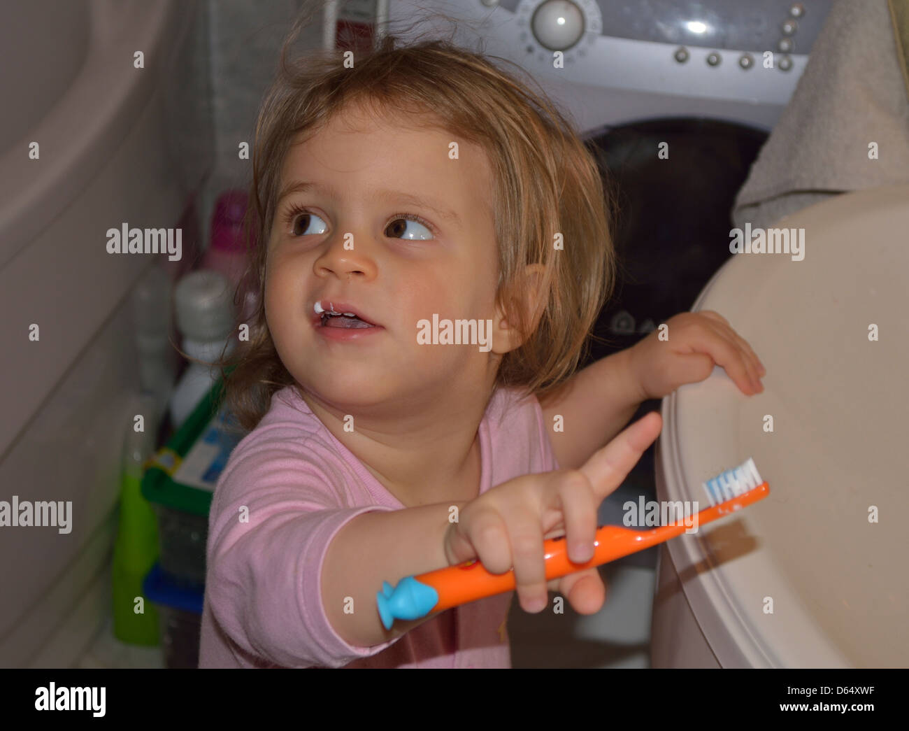 Little girl brushing teeth at sink with toothpaste on upper lip Stock
