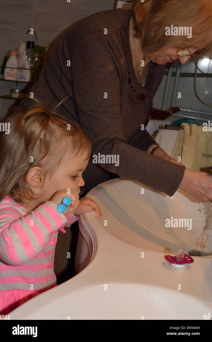 Little girl brushing teeth at sink with Grandmother Stock Photo