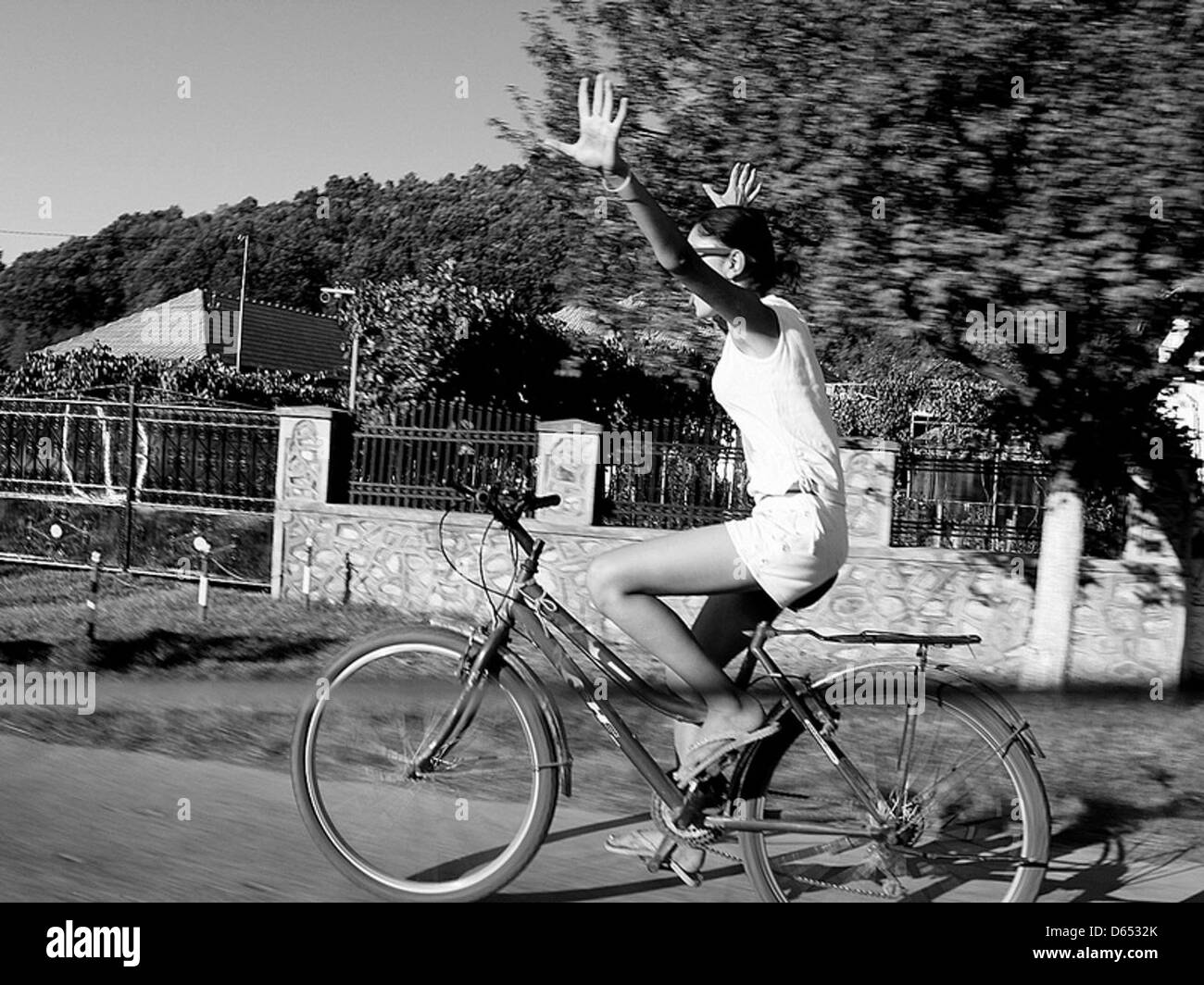 A black-and-white photograph of a girl riding a bicycle on a country road. The photo captures the peaceful rural atmosphere and the simplicity of outdoor life. Stock Photo