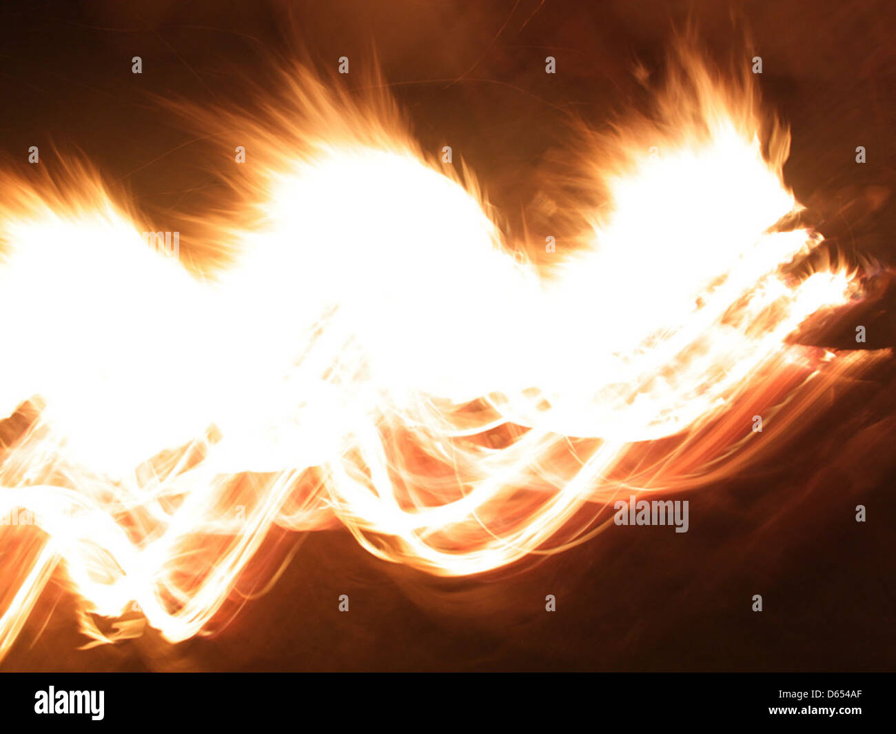 Flames from a campfire flicker in the night, creating a warm glow against the dark backdrop. This image evokes the cozy, comforting atmosphere of a campfire. Stock Photo