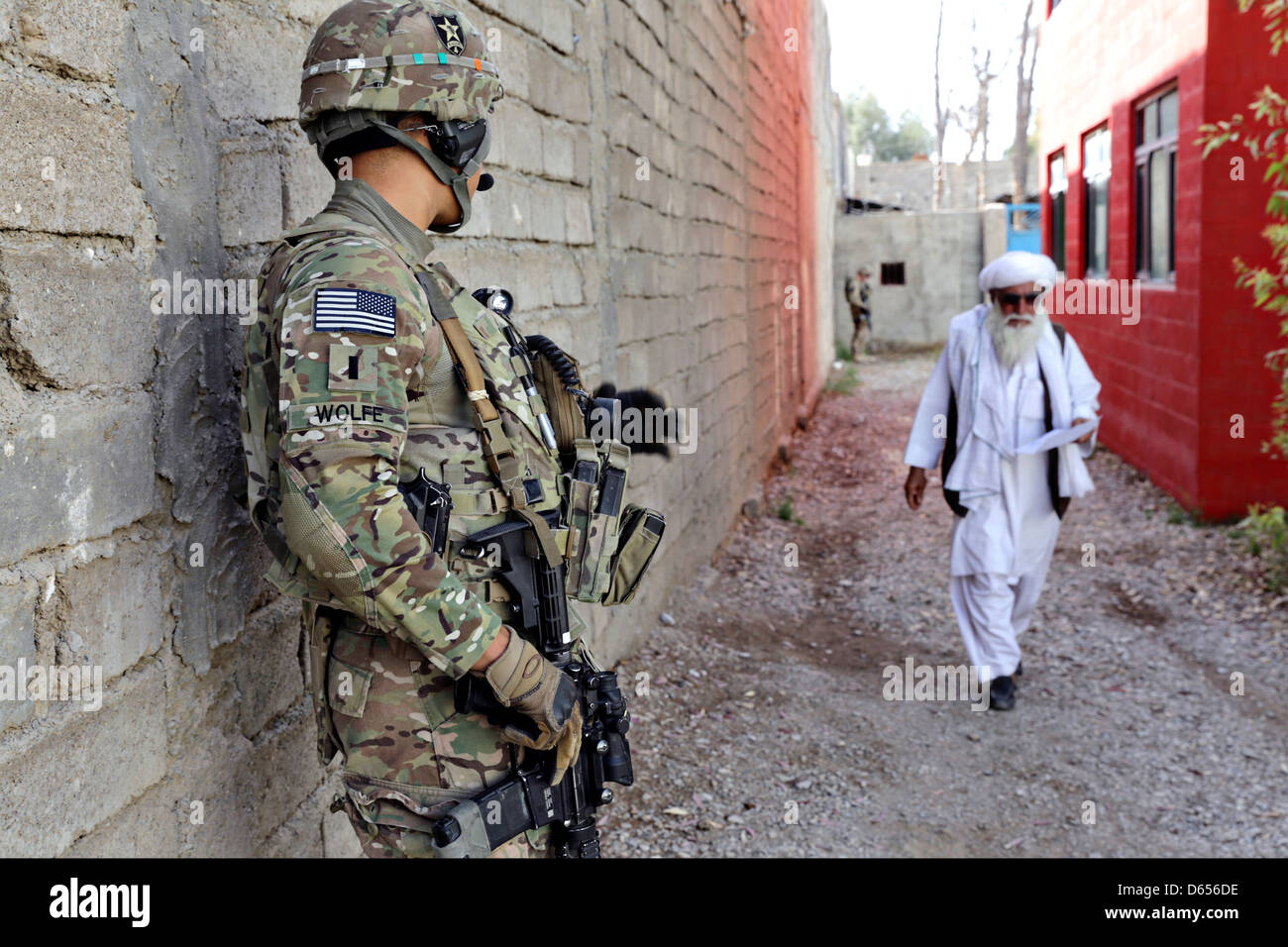 A US Army soldier assigned to the Farah Provincial Reconstruction Team security force watches an elderly Afghan man walk down an alley April 10, 2013 in Farah city, Farah province, Afghanistan. Stock Photo