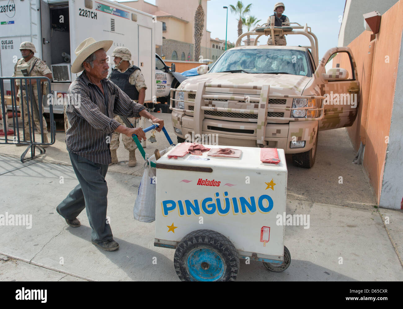 Ein Eisverkäufer schiebt am Sonntag (17.06.2012) in Los Cabos, Mexiko, seinen Eiswagen an bewaffneten Soldaten vorbei. Am 18. und 19.06.2012 findet in dem exklusiven Badeort am Pazifik der diesjährige G20-Gipfel statt. Foto: Peer Grimm dpa Stock Photo