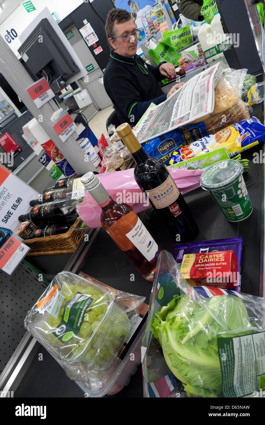 A male employee working at the checkout counter filled with groceries food in Co-Op supermarket Wales UK Stock Photo