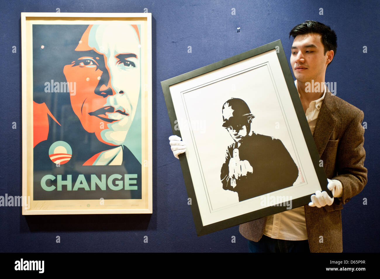 London, UK. 12th April 2013. a sales assistant holds a  canvas entitled “Rude Copper” by Banksy during the 'Urban Art' auction preview at Bonhams. On the left a work entitled 'Change' by Shepard Fairey Credit: Piero Cruciatti / Alamy Live News Stock Photo