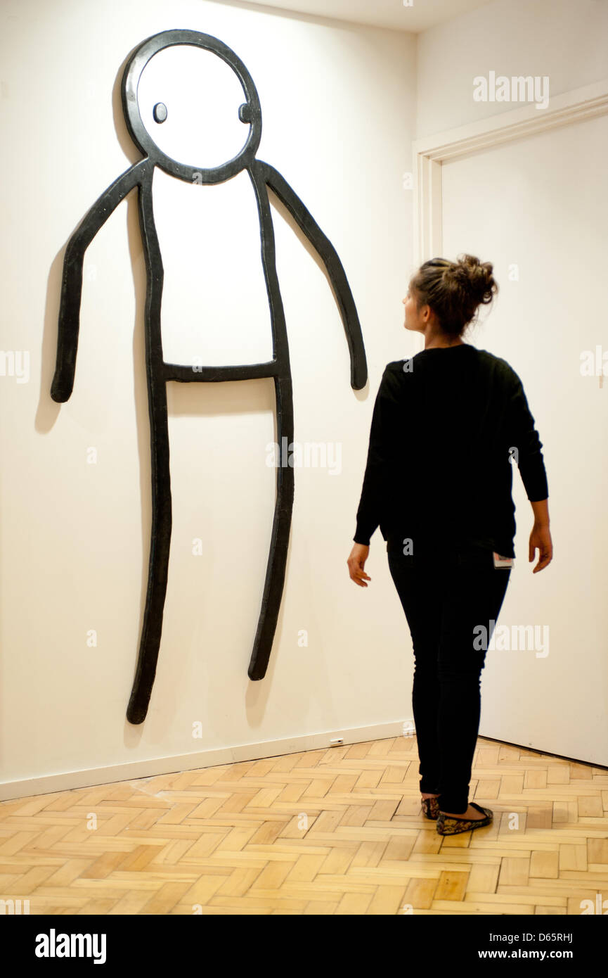 London, UK. 12th April 2013. a sales assistant poses for a picture next to work by Stik entitled 'Stick on wood' by 65 AR W during the 'Urban Art' auction preview at Bonhams. Credit: Piero Cruciatti / Alamy Live News Stock Photo