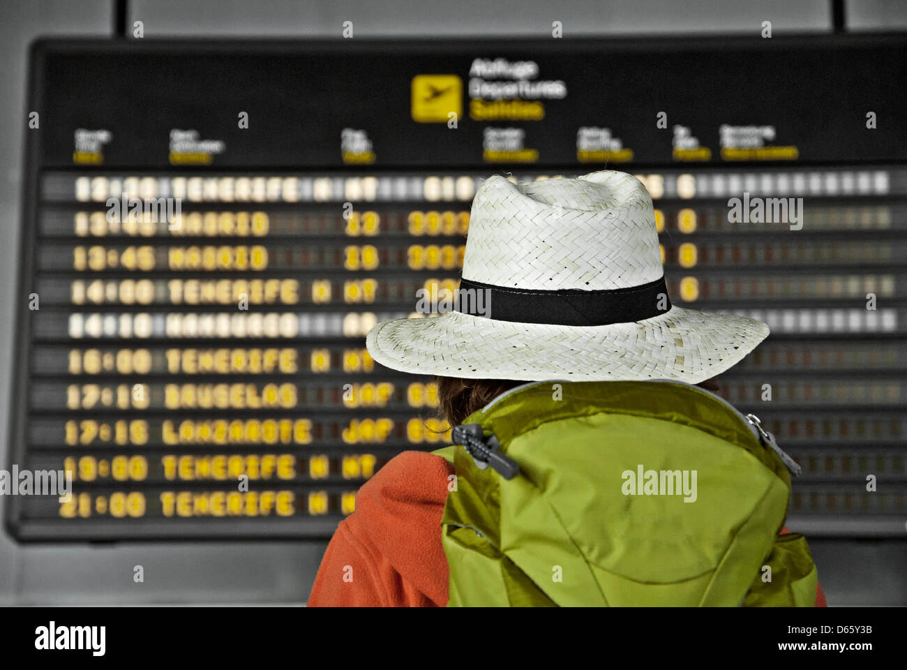 Teenager with backpack and straw hat looks at the scoreboard in an airport. Stock Photo