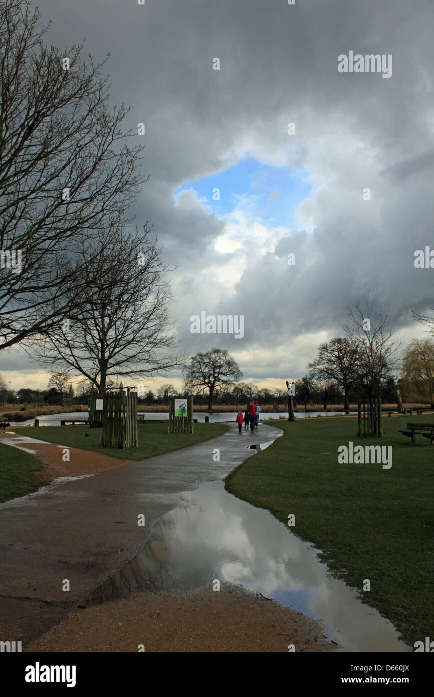 Bushy Park, SW London, England, UK.  12th April 2013. Stormy skies and heavy rain were the latest weather conditions in Southern England today. This family take a walk by the Heron Pond between the showers. Credit: Julia Gavin / Alamy Live News Stock Photo