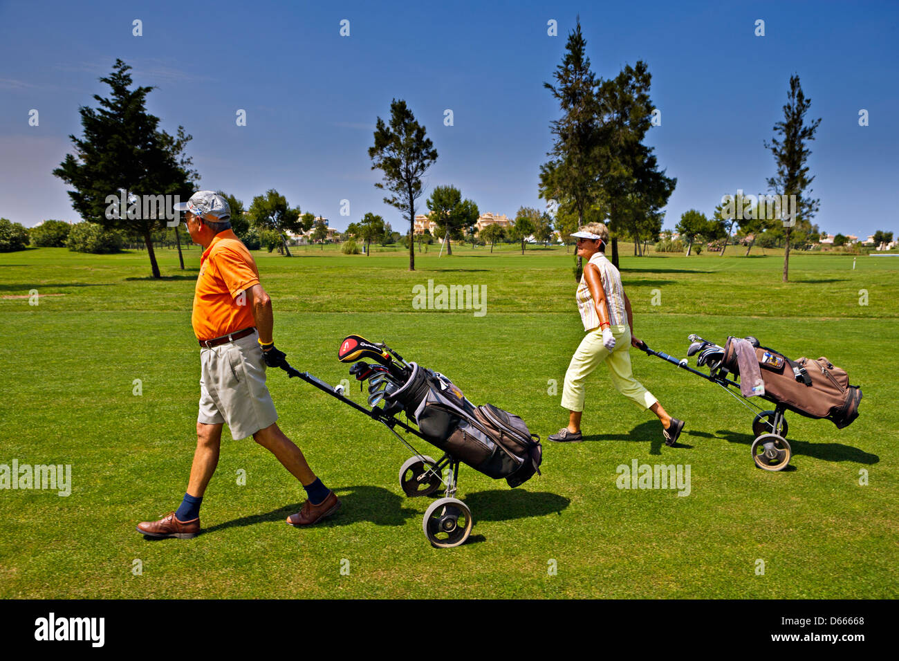 Couple walking with their golf carts at the Oliva Nova Golf Course, Club de Golf Oliva Nova, an 18 hole golf Course. Stock Photo