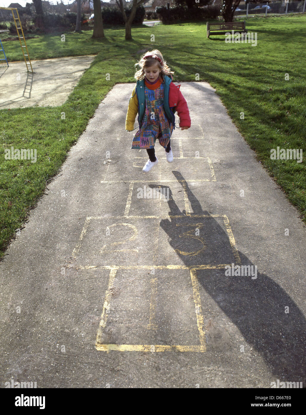 Young girl (5yrs) playing hopscotch in playground, Winkfield, Berkshire, England, United Kingdom Stock Photo