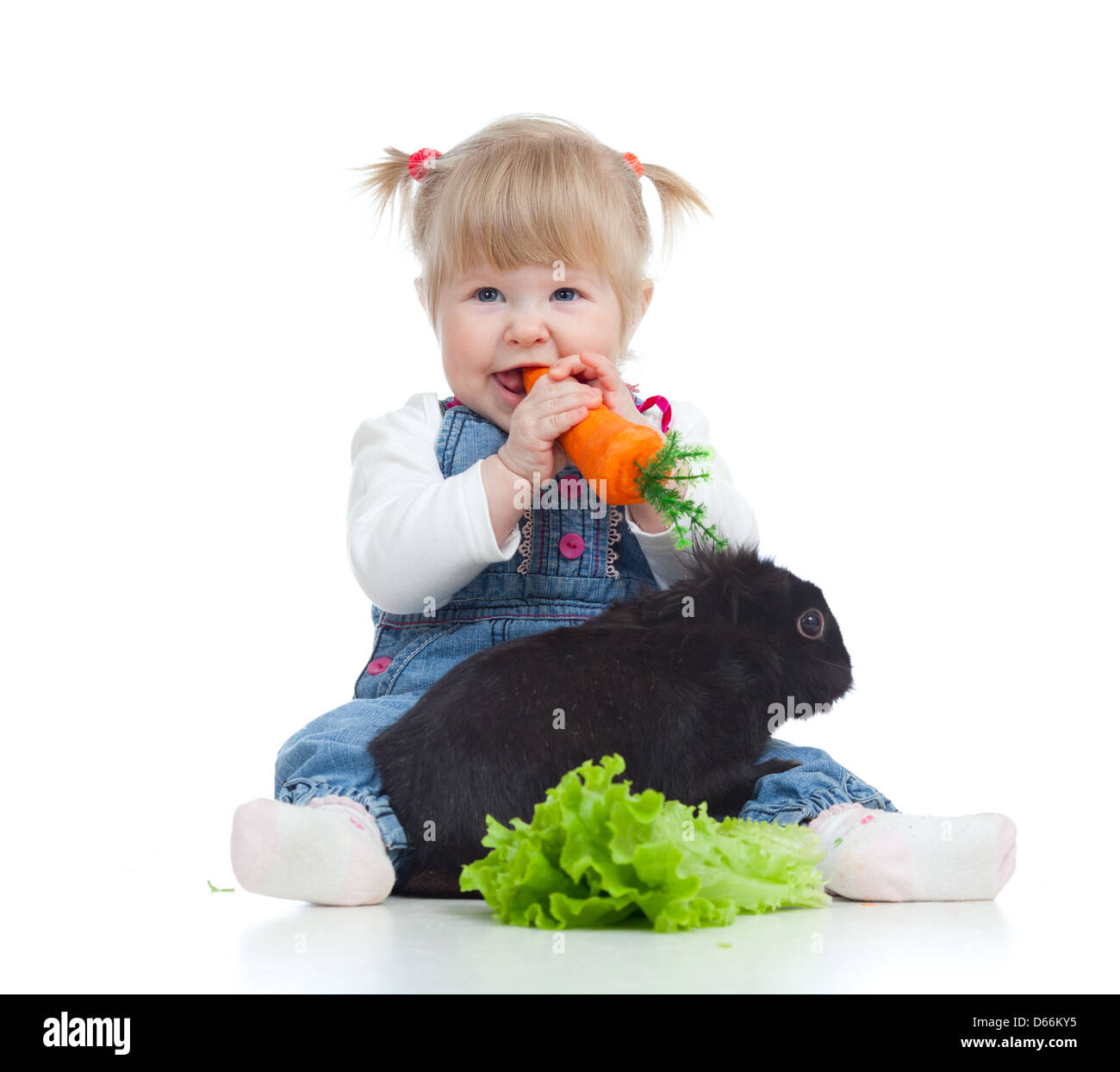 Smiling little girl eating a carrot and feeding rabbit with lettuce on ...