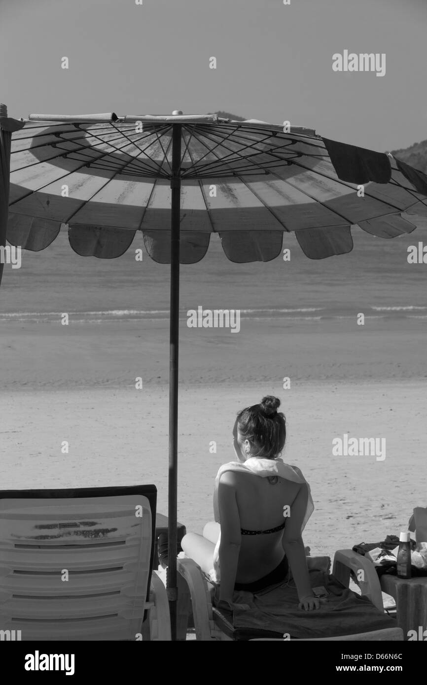Sunbathing tourist sits under beach umbrella, Thailand Stock Photo